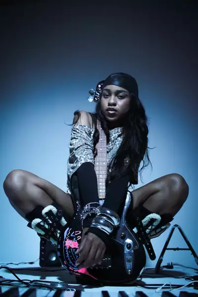 Amatiime crouching on the floor surrounded by wires, on a blue background