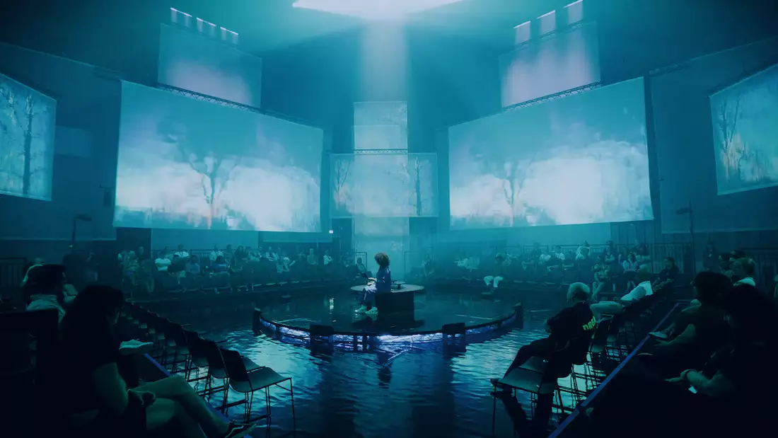 The set of A Symphony of Flesh and Bones in the Warehouse, showing projections on large screens and pieces of fabric. The lighting is blues-green.