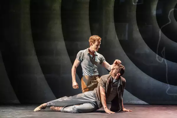 A photo of two ballerinas, one lying on the ground the other leaning over him