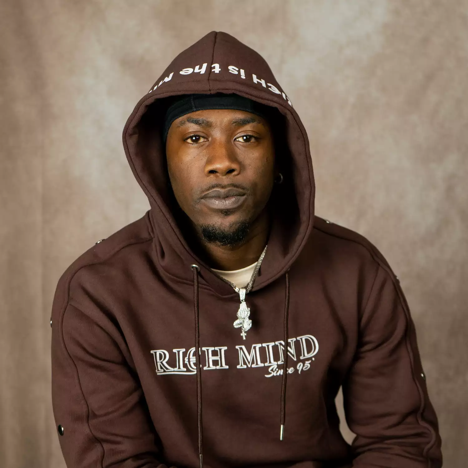 Headshot of Edzor Talez wearing a brown hooded sweatshirt that reads "rich mind"