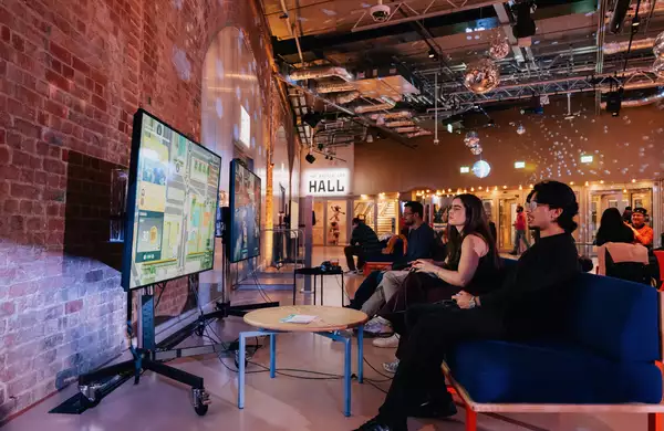 Two people playing on the playstation in the Social. The lighting is dim and disco balls are on display.