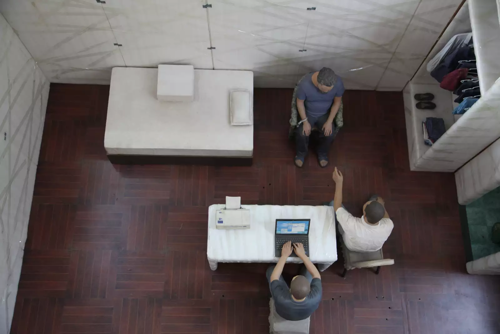 A diorama showing Ai Weiwei in secret detention, sat in a chair with two guards interrogating him