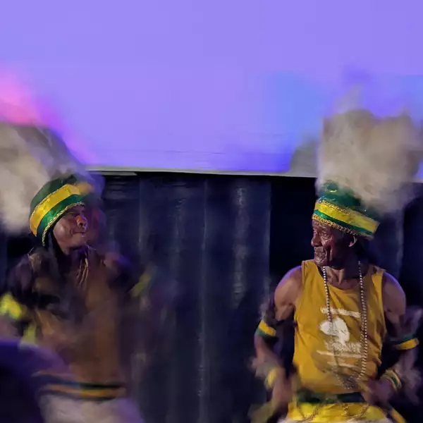 Two men playing drums wearing hats in Brazil flag colours. The sky is purple.